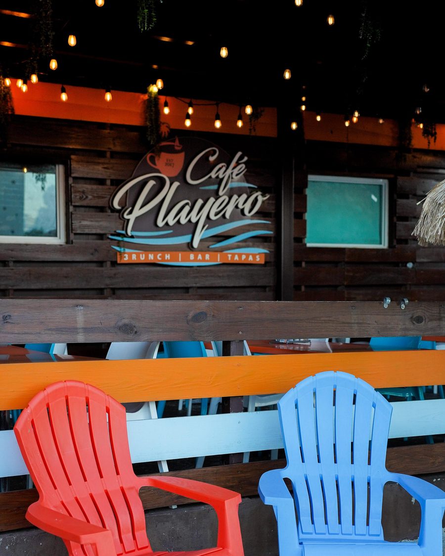 La terraza de Café Playero, con sillas de playa de colores bajo las luces y el letrero